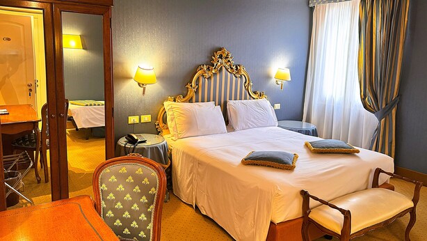 A hotel room with a large bed, two bedside lamps, a wooden chair, a desk, and a mirror. - Hotel Corte Contarina (Venice)