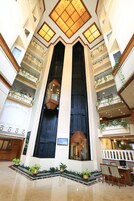 A hotel lobby with a central staircase, multiple balconies with plants, and a reception desk.