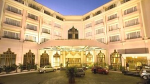 A multi-story hotel with a central courtyard, featuring a grand entrance with a canopy, several balconies, and a well-maintained lawn. - The Chancery Hotel (Bengaluru)