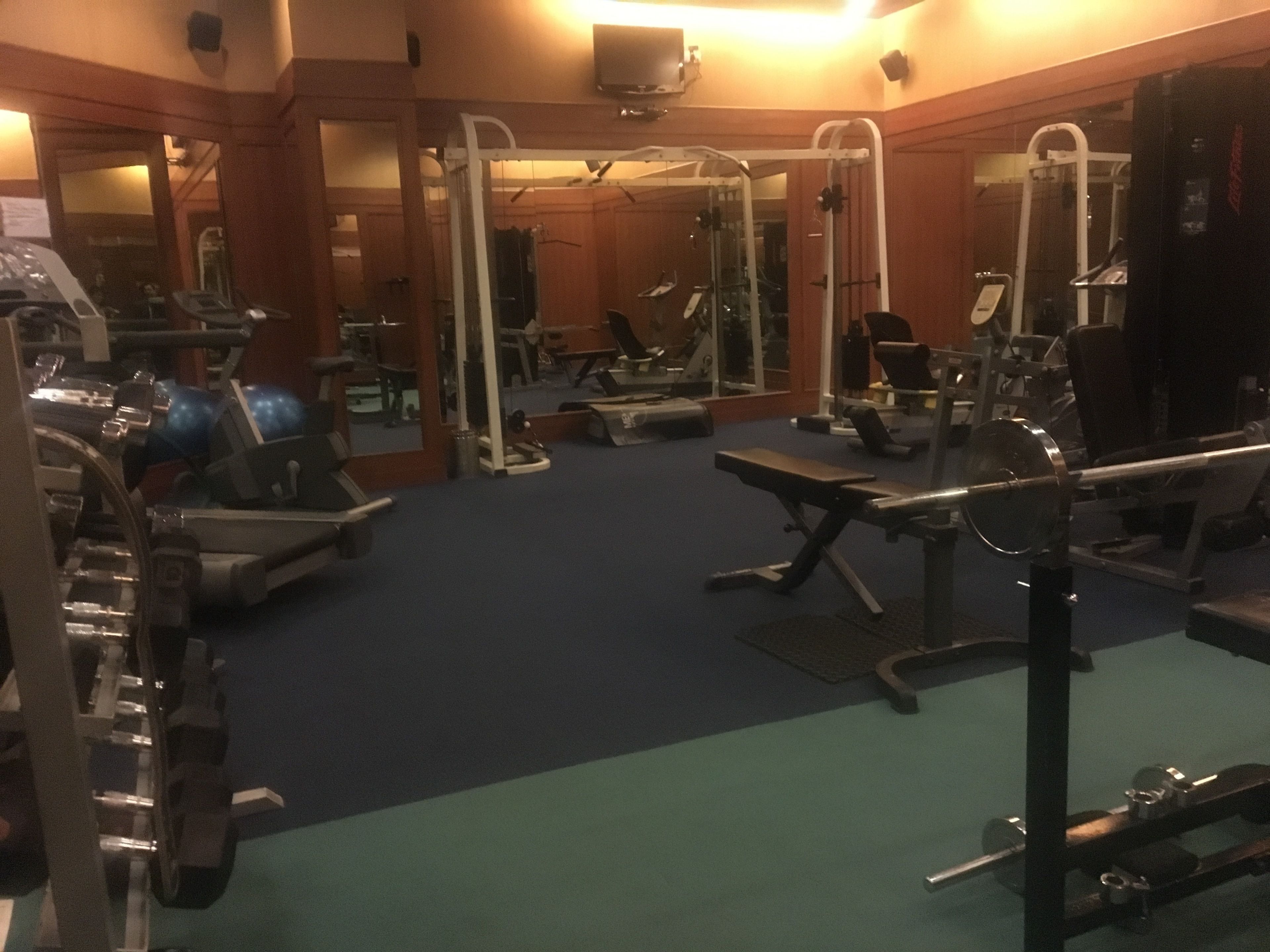 Un gimnasio con diversos equipos de ejercicio, espejos y una alfombra azul.