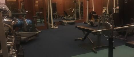 Un gimnasio con diversos equipos de ejercicio, espejos y una alfombra azul.