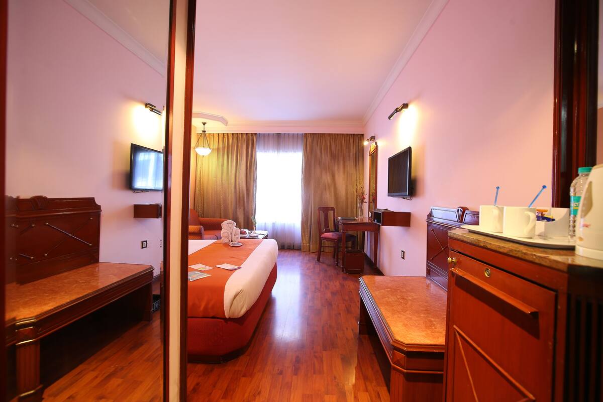 A hotel room with a bed, desk, chair, and a television on the wall.