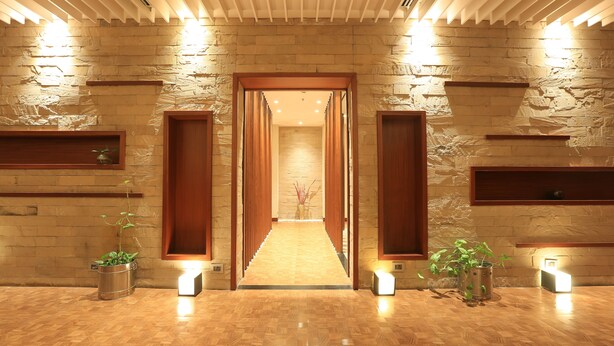 A hallway with a stone wall, wooden doors, and potted plants. - The Chancery Hotel (Bengaluru)