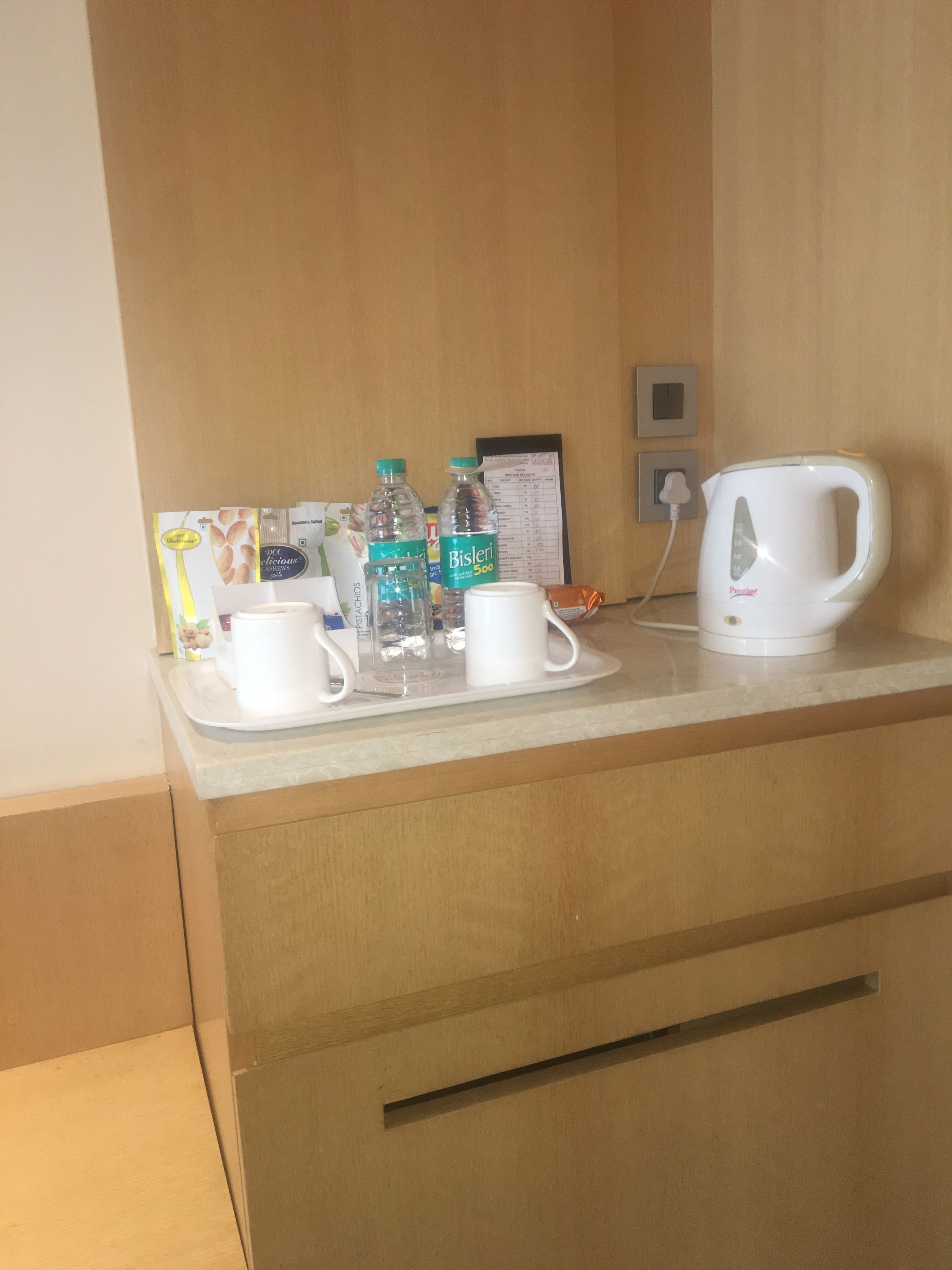 Mostrador de hotel con una bandeja de vasos blancos, botellas de agua Bisleri y una tetera eléctrica blanca.