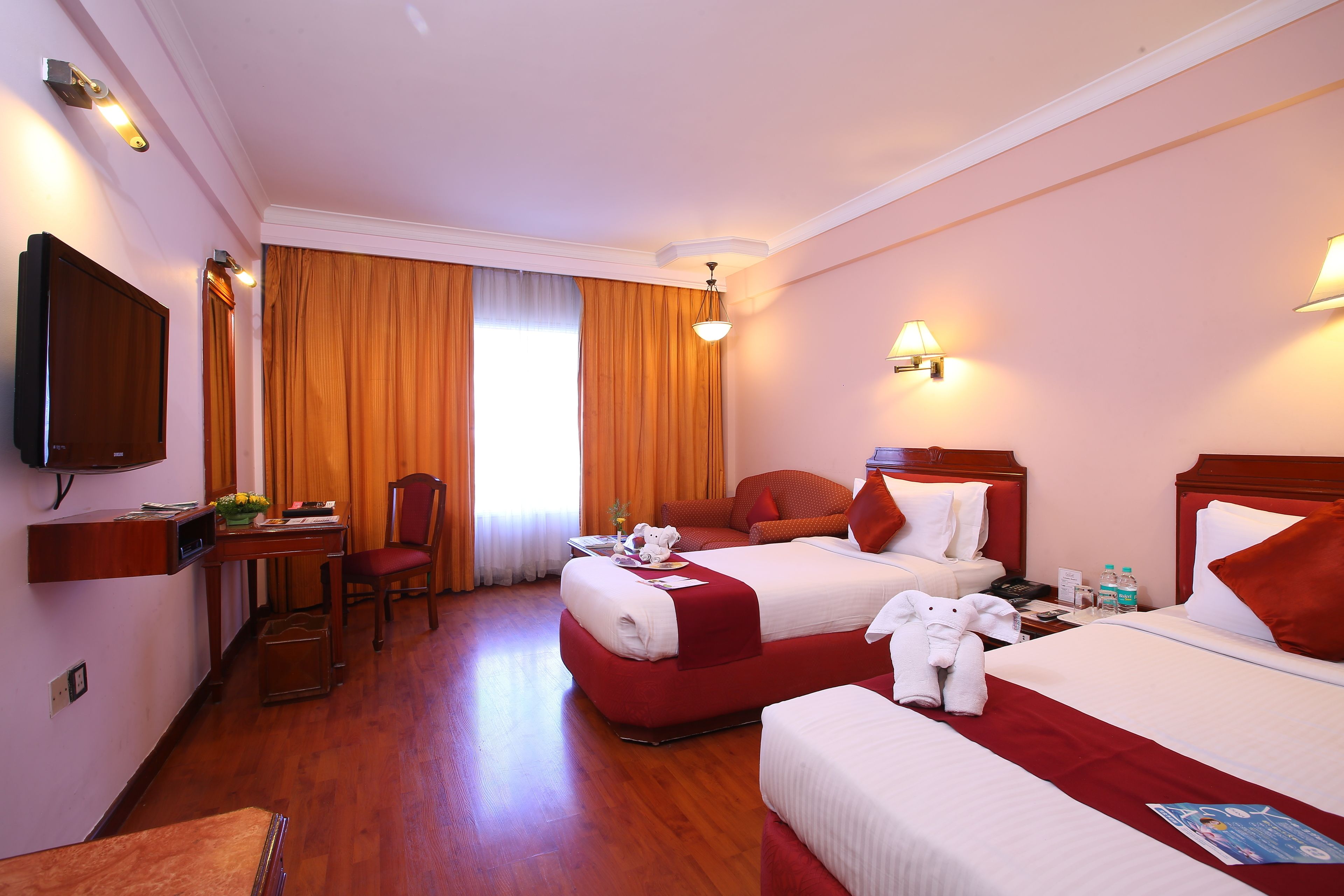 Habitación de hotel con dos camas, un escritorio, una silla, un televisor y una ventana con cortinas.