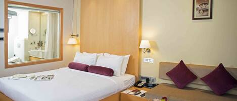A hotel room with a large bed, a bedside table with a lamp, a small sofa, and a framed picture on the wall.