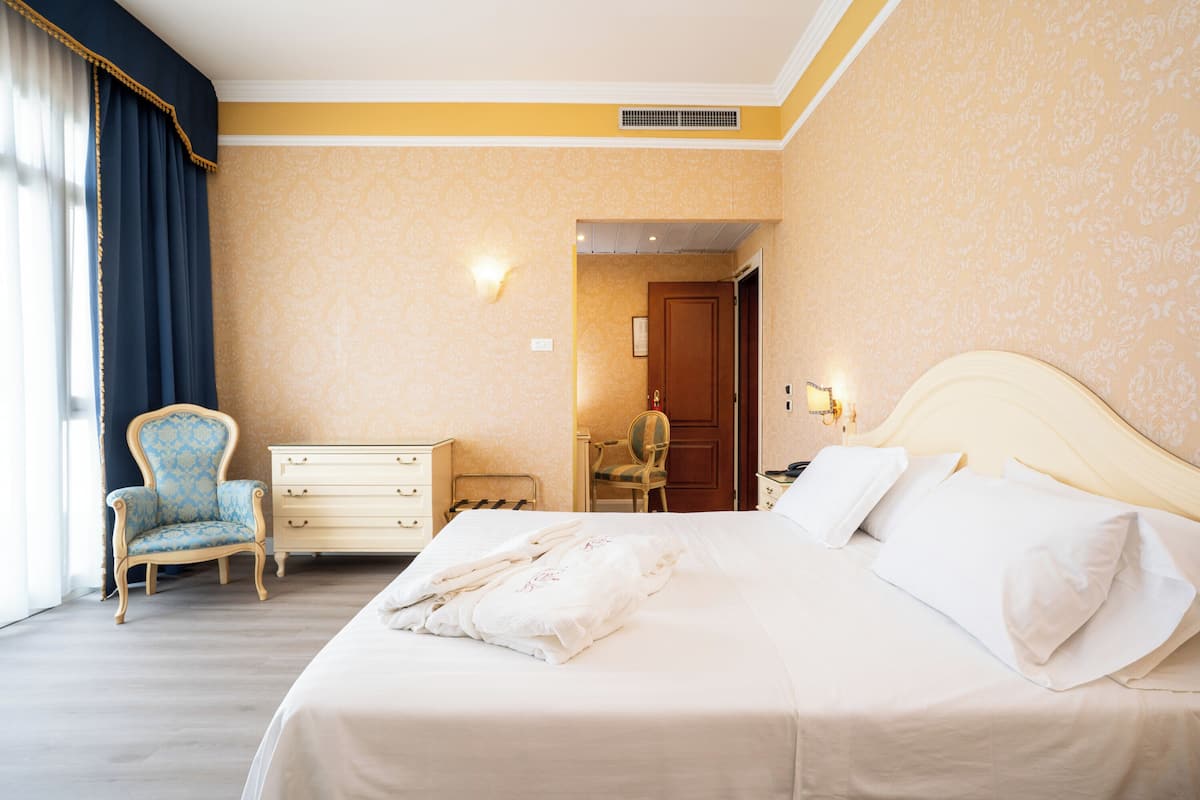 Una habitación de hotel con una cama, una silla, un aparador y una puerta que da a un baño.