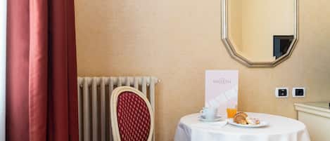 Habitación de hotel con una silla roja, una mesa con desayuno, un espejo y un radiador.