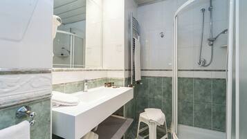 Ein Badezimmer mit einem weißen Waschbecken, einem Spiegel, einer Dusche mit Glastür und einem kleinen Hocker.