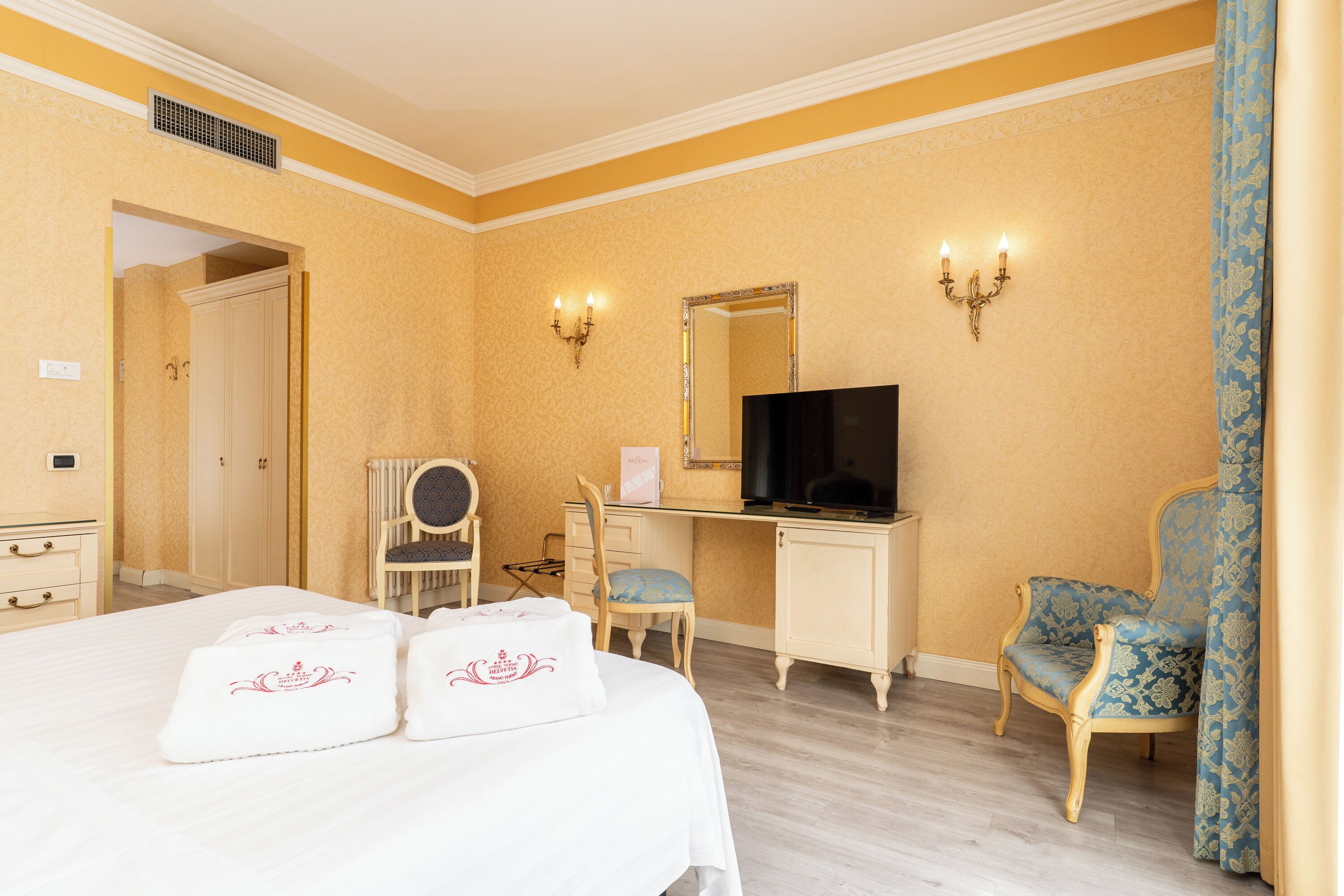A hotel room with a bed, a desk, a television, and two chairs.