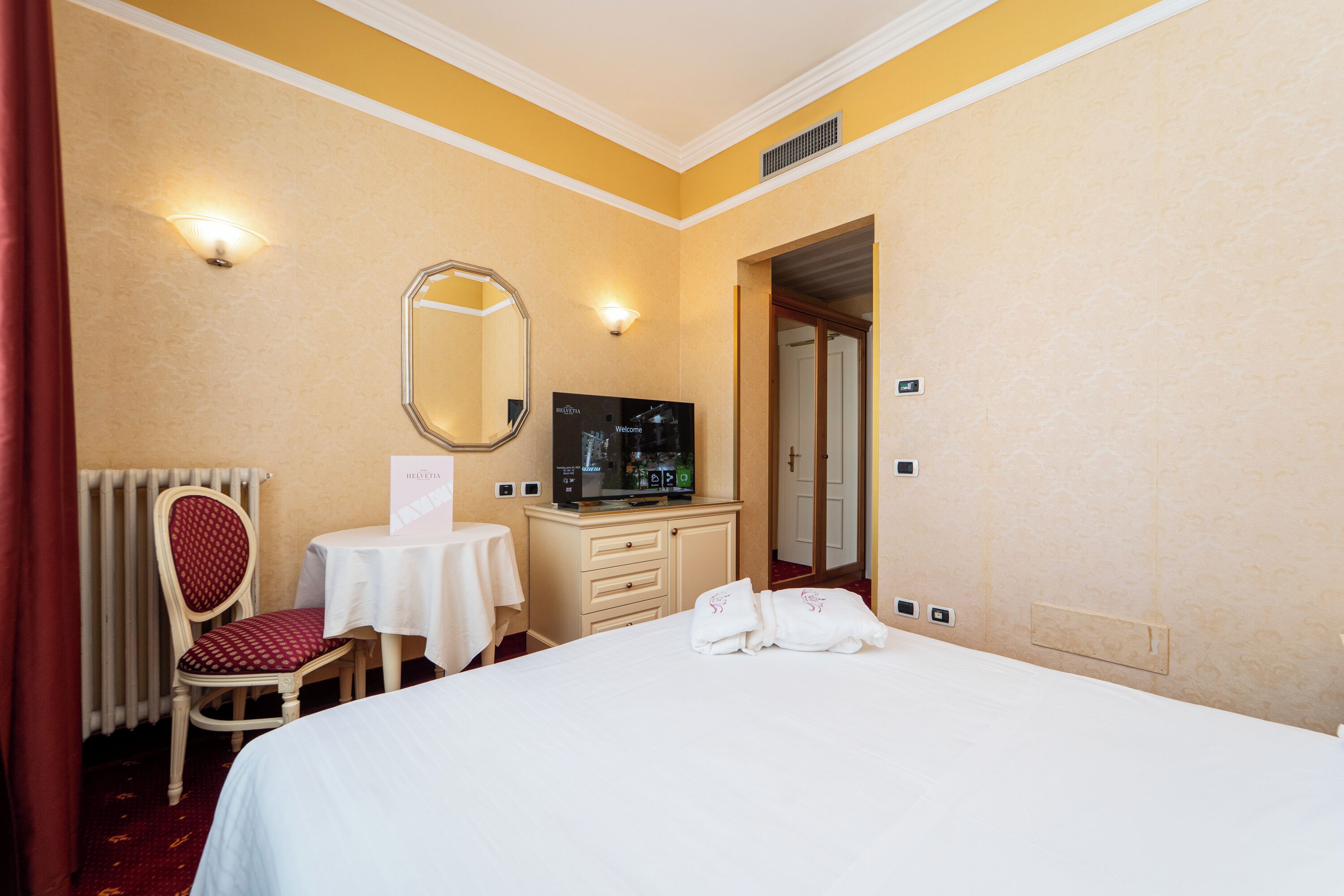 Een hotelkamer met een bed, een televisie, een bureau met stoel en een spiegel.