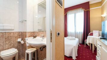 A hotel room with a bathroom, a bed, a desk, and a television.