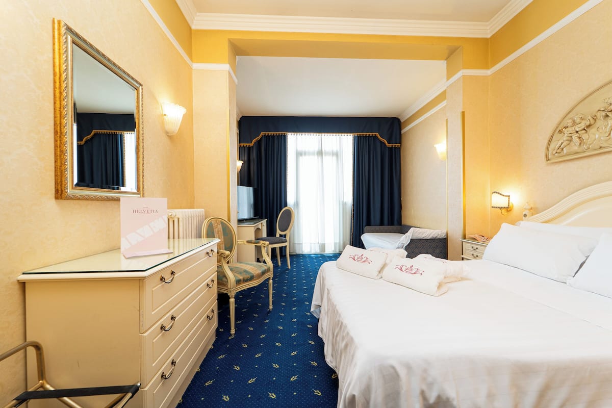 Una habitación de hotel con cama, escritorio, silla, cómoda y espejo.
