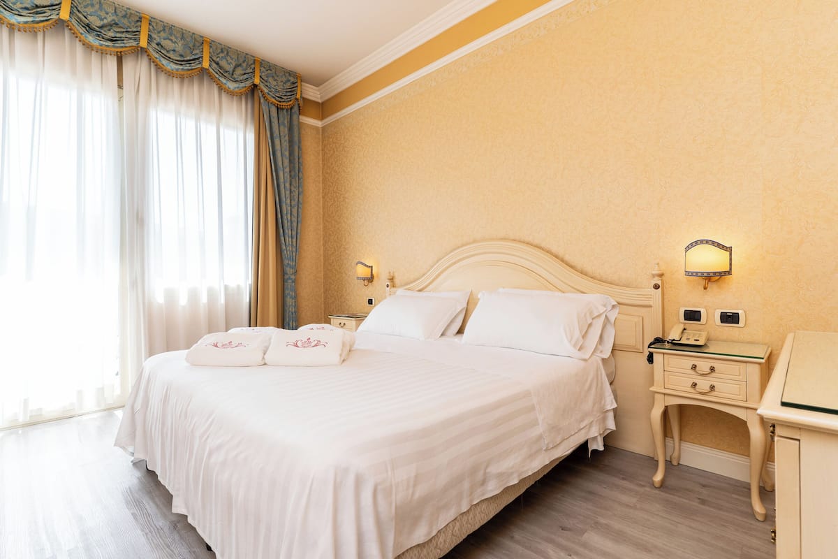 Habitación de hotel con una cama grande, una mesita de noche con lámpara, otro mesita y teléfono fijo en la pared.