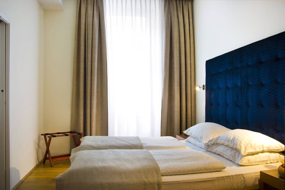 A hotel room with a large bed, two bedside tables, a small wooden side table, and a window with curtains.