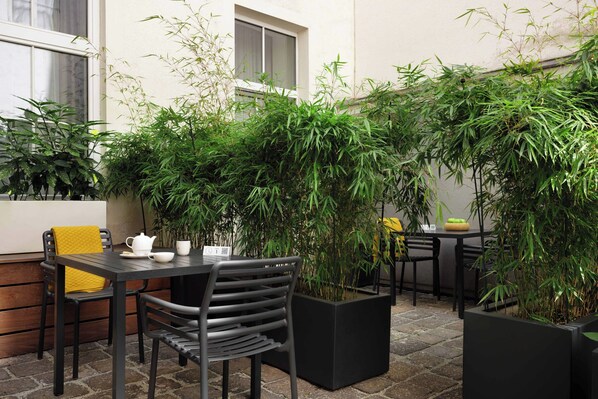 Uma área de pátio ao ar livre com mesa e cadeiras, cercada por grandes vasos de plantas.