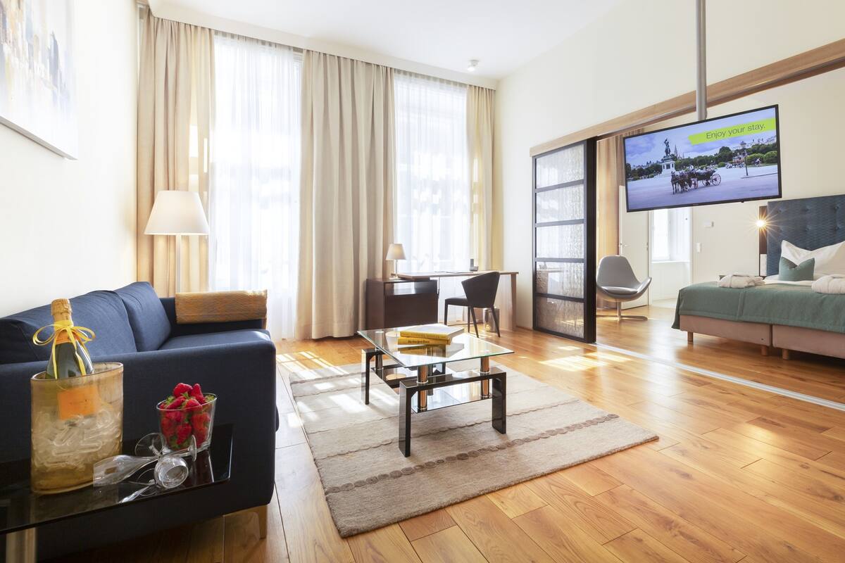 A modern hotel room with a large bed, a sofa, a coffee table, and a TV displaying a scenic view.
