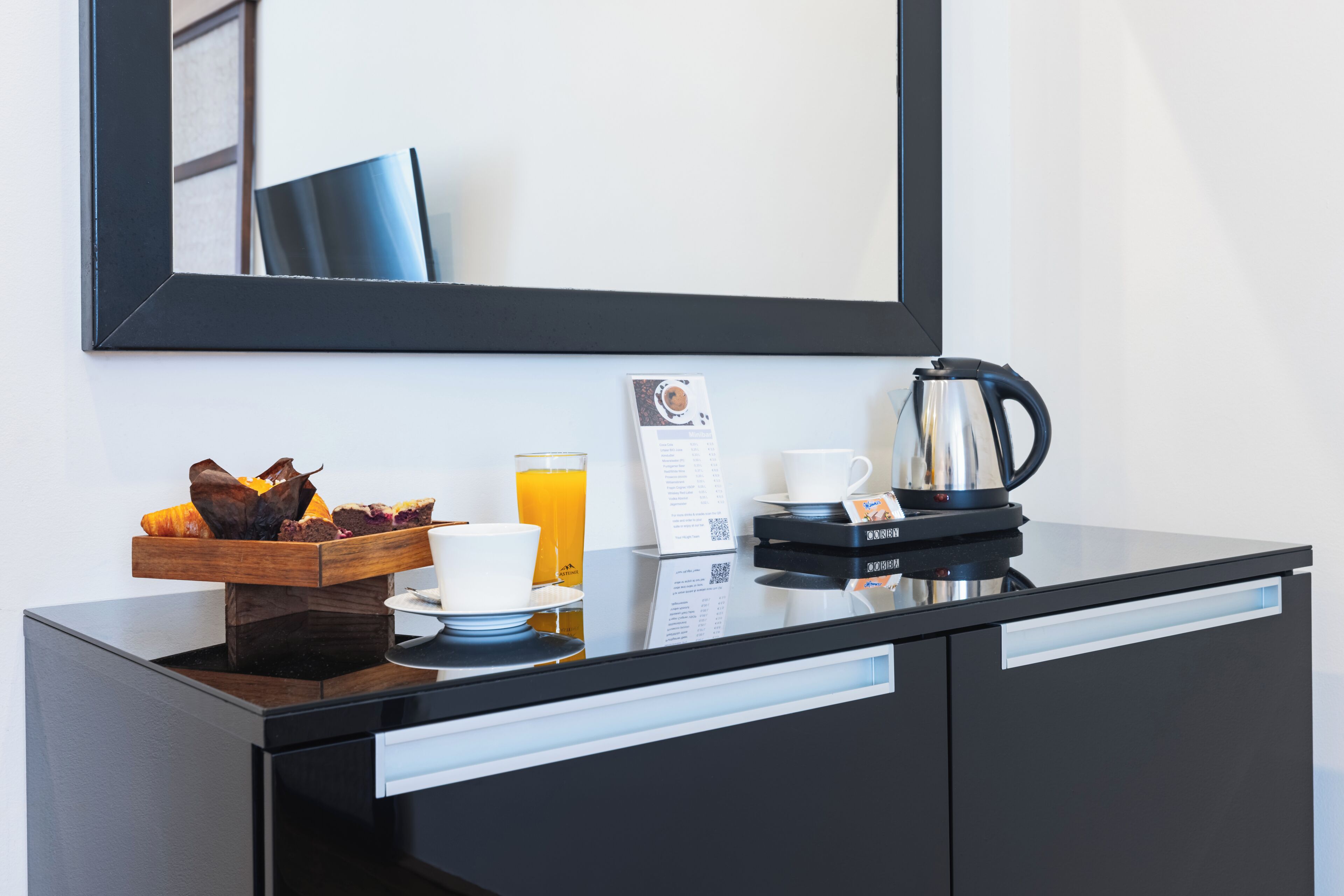 Quarto de hotel com minibar preto, cafeteira, copo de suco de laranja, prato de pastelaria e menu.