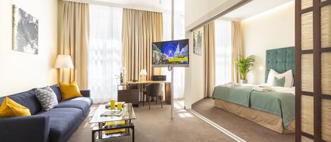 A hotel room with a sofa, a bed, a desk, a TV, and a window with curtains.