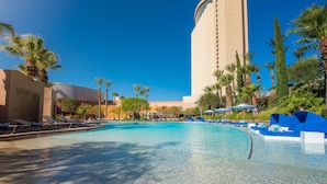 A swimming pool with lounge chairs and umbrellas, surrounded by palm trees and a tall building. - Morongo Casino Resort Spa (Cabazon)