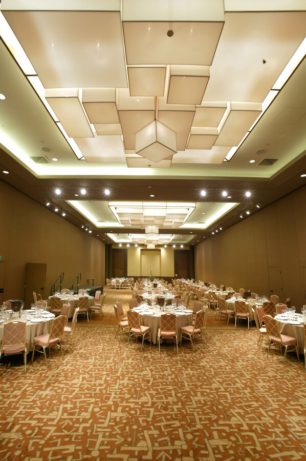 A large banquet hall with round tables and chairs, a patterned carpet, and a modern ceiling design.