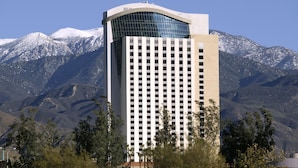 A tall hotel with a modern design, featuring a curved glass facade and a grid of windows. It is situated in a mountainous area with snow-capped peaks in the background. - Morongo Casino Resort Spa (Cabazon)
