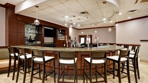 Zona de bar con una isla central, taburetes, luces colgantes y una barra con botellas.