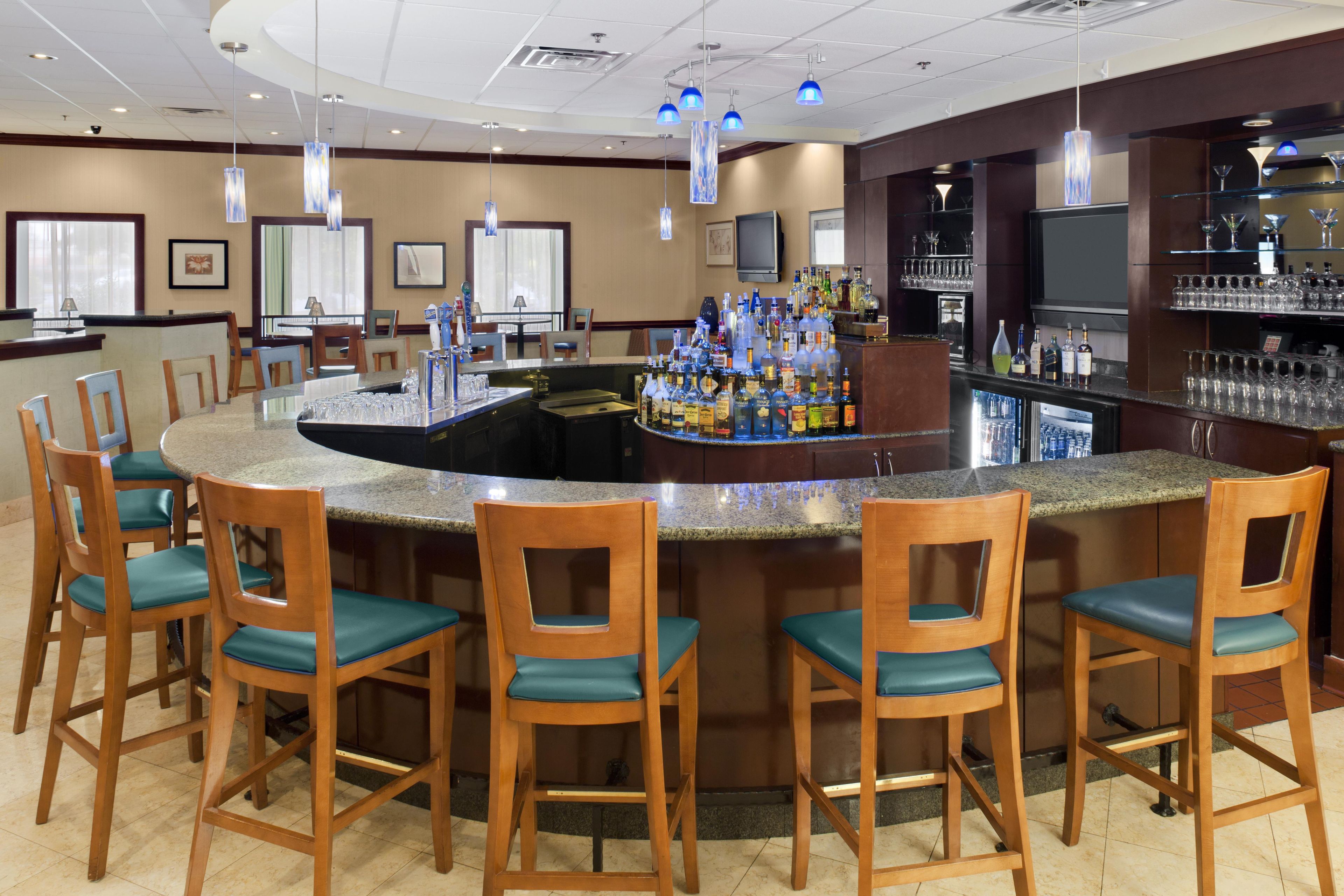 A bar area with a curved counter, bar stools, and a variety of bottles and glasses.