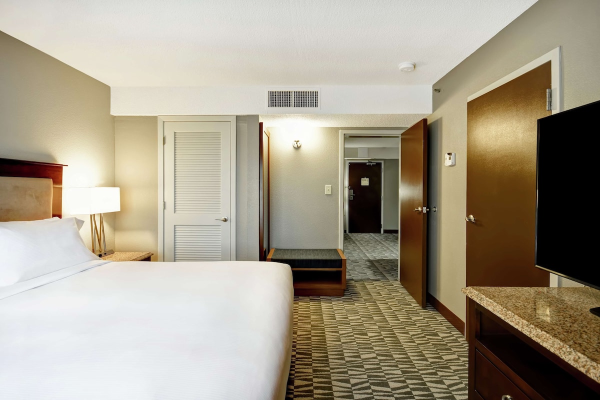 A hotel room with a bed, a TV, a desk, and a bathroom door.