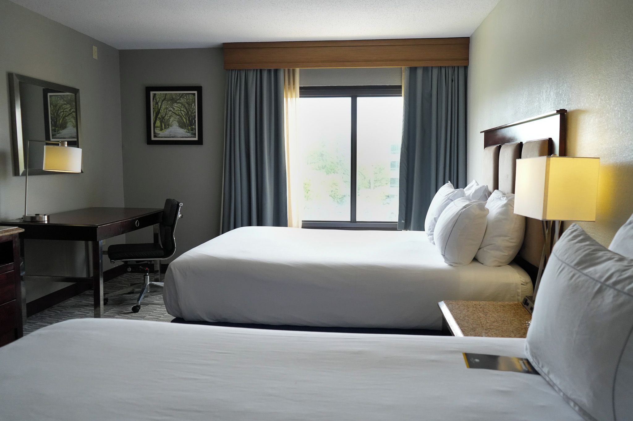 A hotel room with two beds, a desk, and a chair.