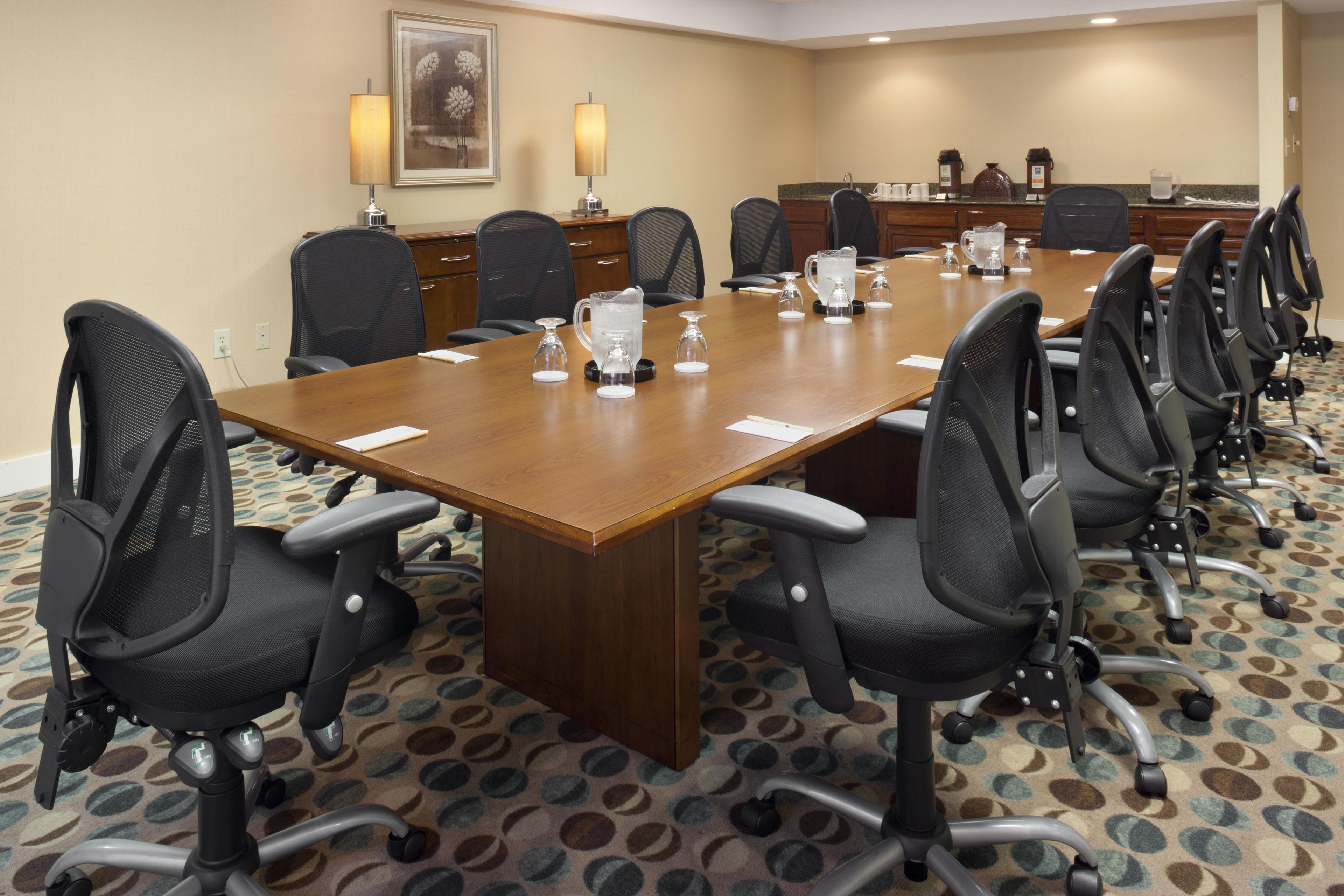 A conference room with a long table, multiple chairs, a coffee station, and a painting on the wall.