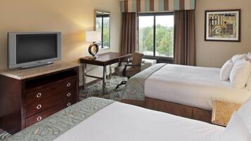 A hotel room with two beds, a desk, a television, and a large window.