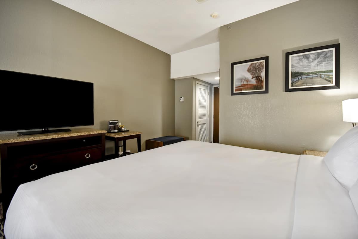 Ein Hotelzimmer mit einem großen Bett, einem Flachbildfernseher, einem kleinen Tisch und zwei gerahmten Bildern an der Wand.