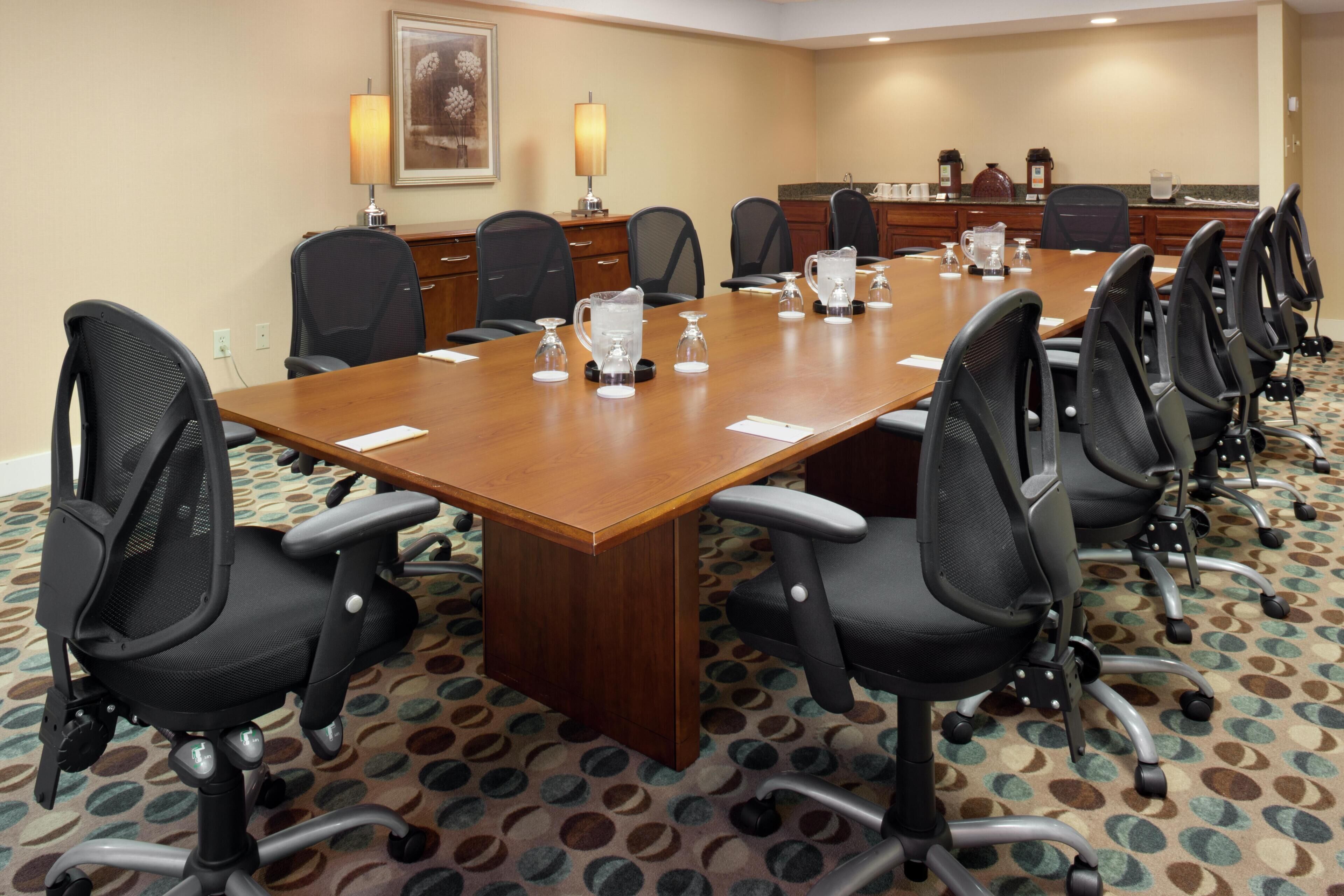 A conference room with a long table, multiple chairs, and a coffee station.
