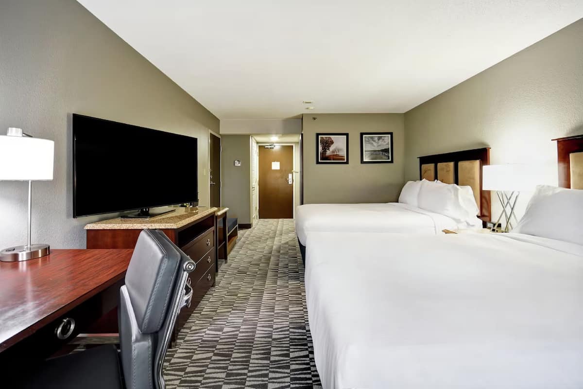 Ein Hotelzimmer mit Bett, Schreibtisch mit Fernseher, Stuhl und einer Tür zu einem weiteren Raum.