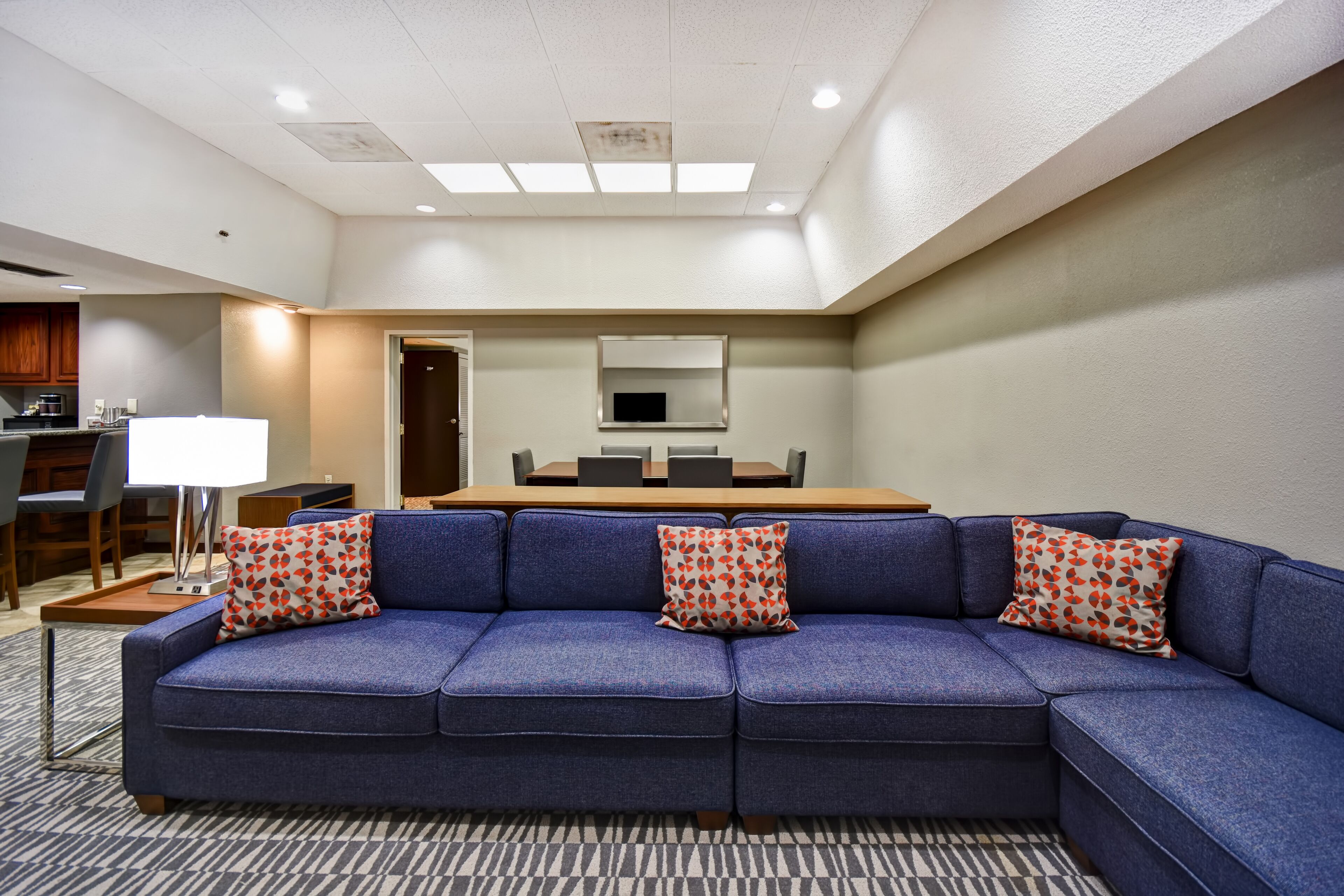 Una habitación de hotel moderna con un sofá seccional azul, una mesa de comedor y un televisor.