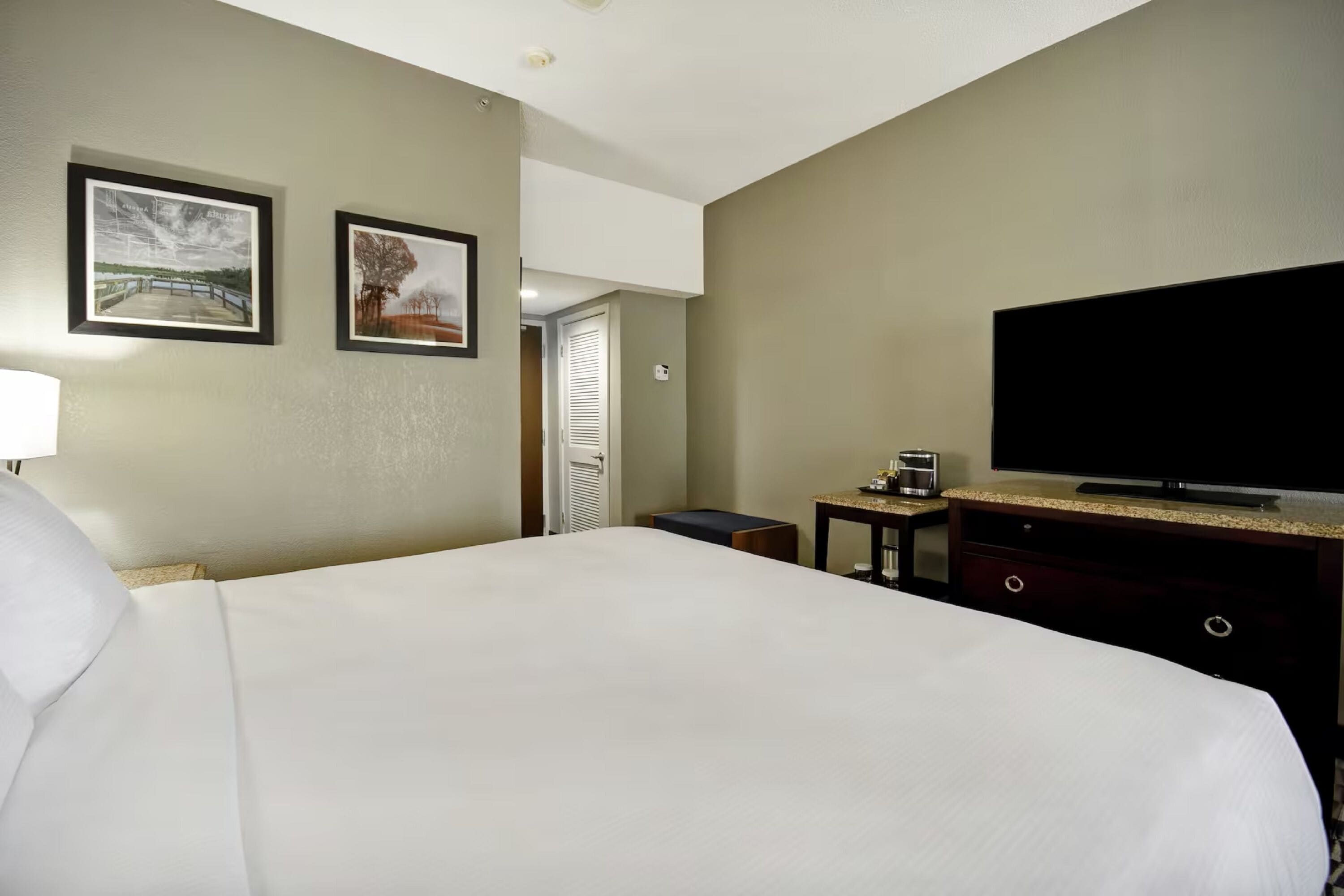 A hotel room with a large bed, a flat-screen TV, a small table, and two framed pictures on the wall.