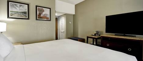 A hotel room with a large bed, a flat-screen TV, a small table, and two framed pictures on the wall.