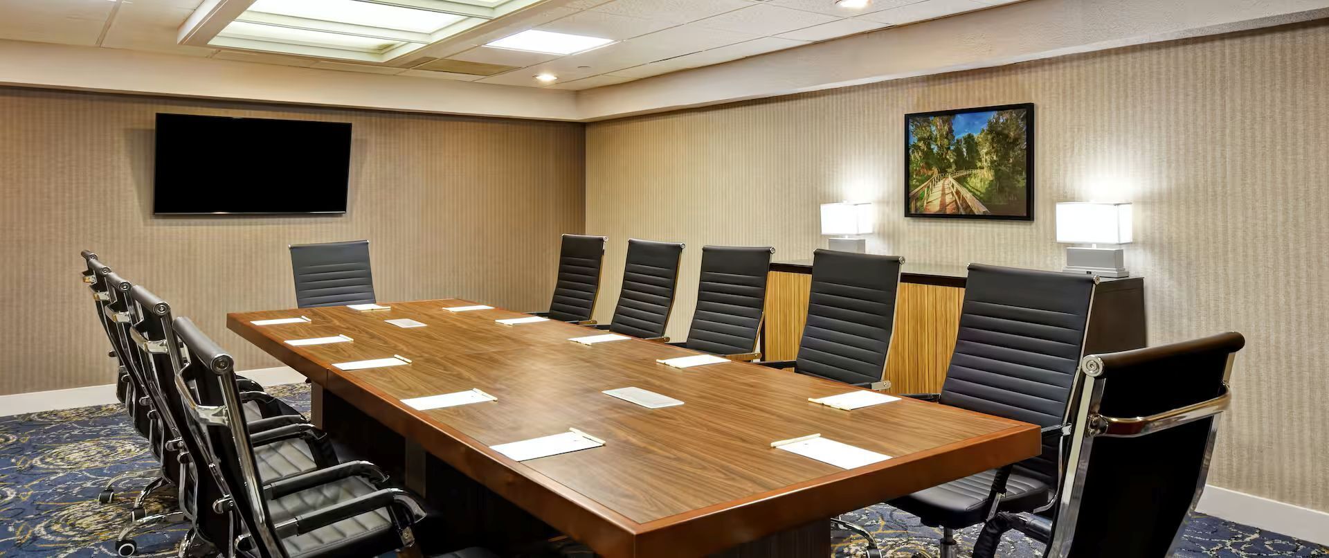 Een vergaderzaal met een lange tafel, meerdere stoelen, een flatscreen-tv en een schilderij aan de muur.
