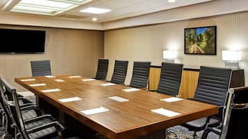 A conference room with a long table, multiple chairs, a flat-screen TV, and a painting on the wall.