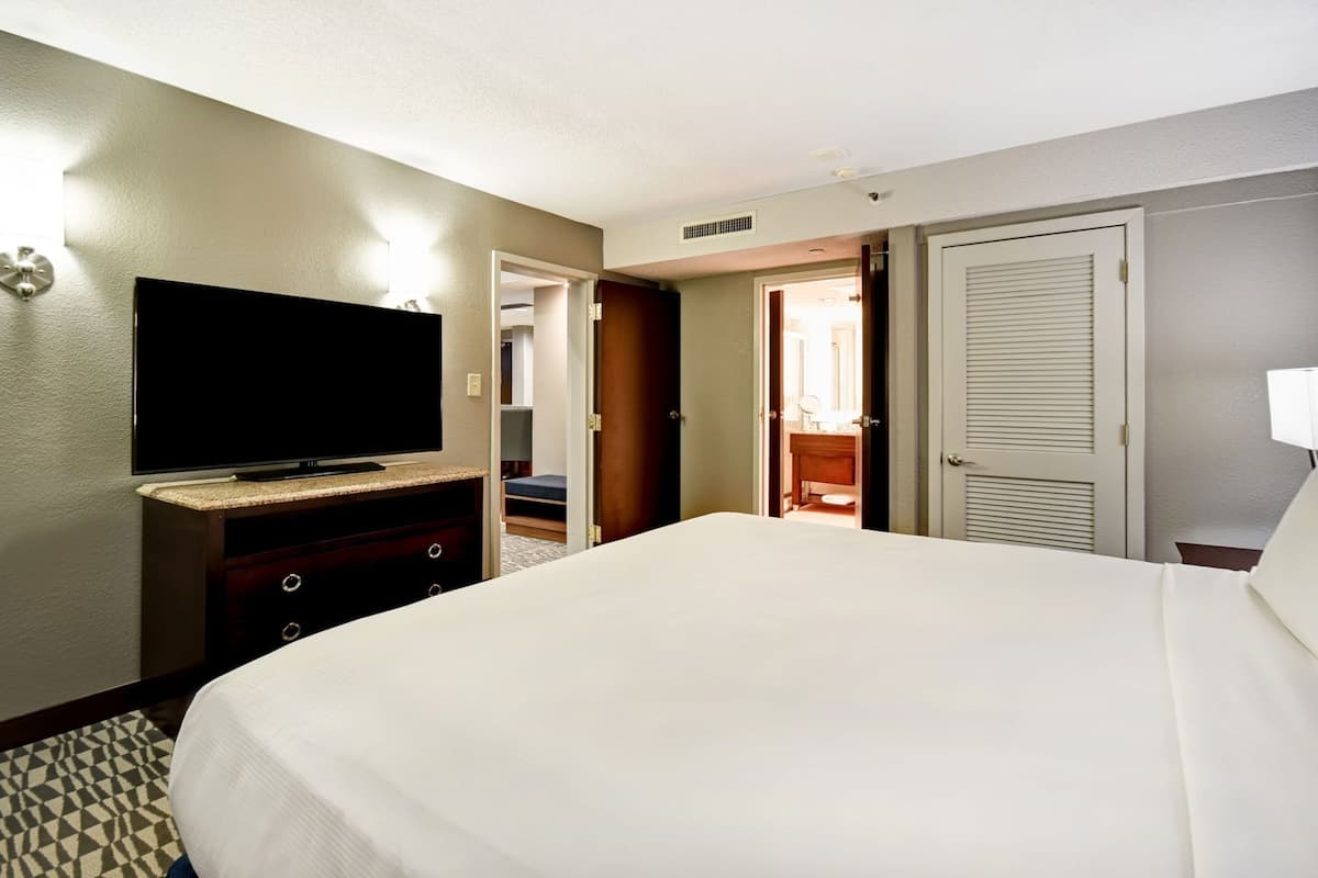 Ein Hotelzimmer mit einem Bett, einem Fernseher auf einer Kommode, einem durchgegangenen Tür erkennbaren Badezimmer und einem Kleiderschrank mit Schiebetür.