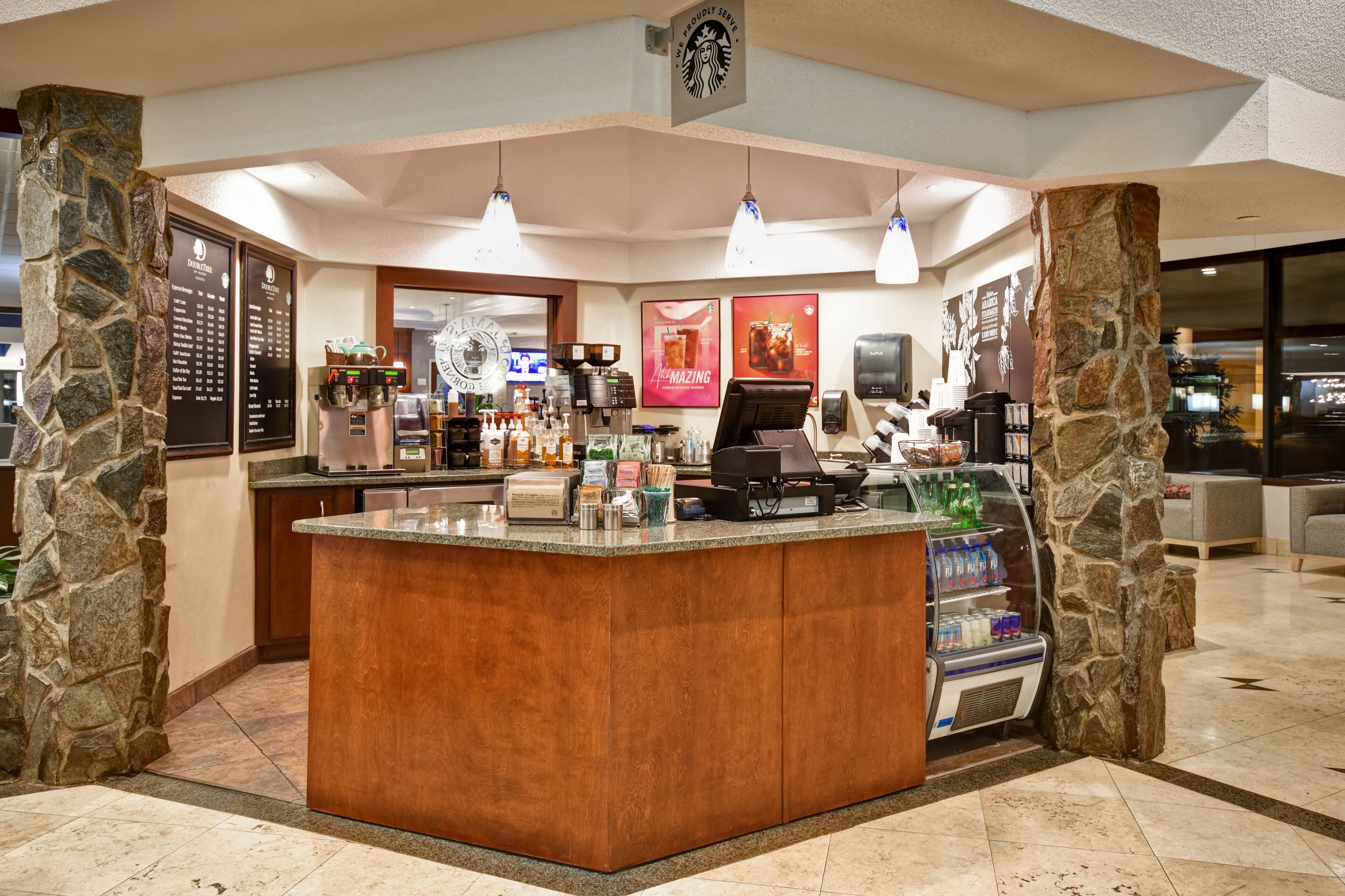 Uma cafeteria Starbucks com balcão de madeira, pilares de pedra e um quadro de cardápio.