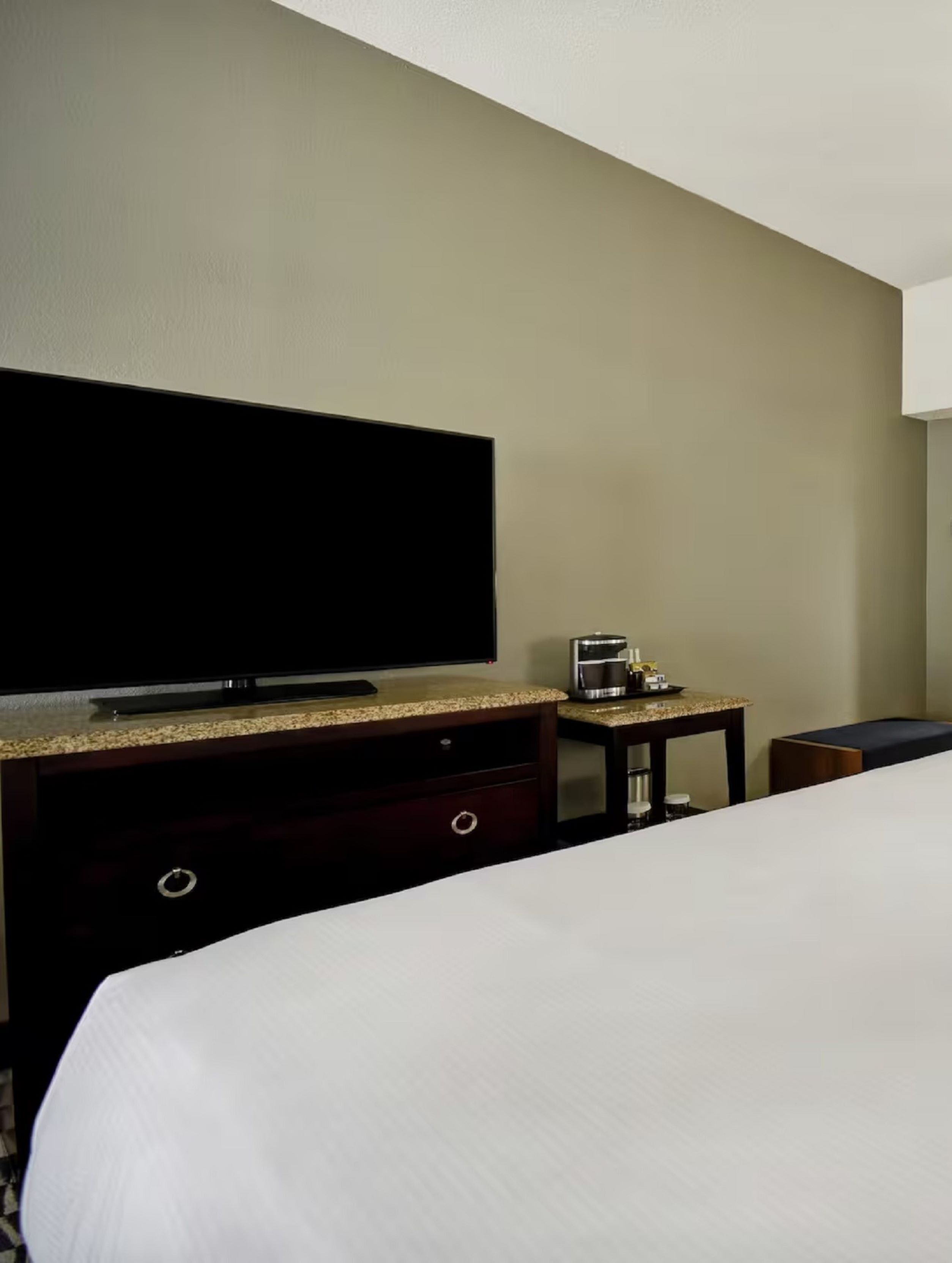 Une chambre d’hôtel avec un grand lit, un téléviseur à écran plat, une machine à café et une petite table.