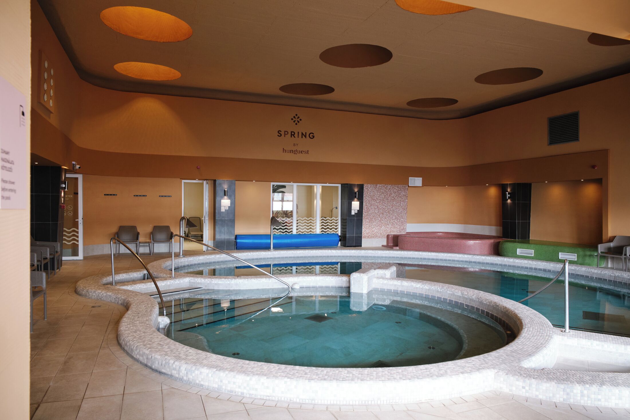An indoor swimming pool with a circular design, a lounge area with seating, and a ceiling with circular light fixtures.