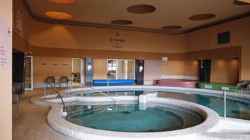 An indoor swimming pool with a circular design, a lounge area with seating, and a ceiling with circular light fixtures.