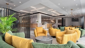 A modern lobby with green and yellow upholstered sofas, a marble coffee table, and a staircase with a glass railing. - Hunguest Hotel Flora (Eger)