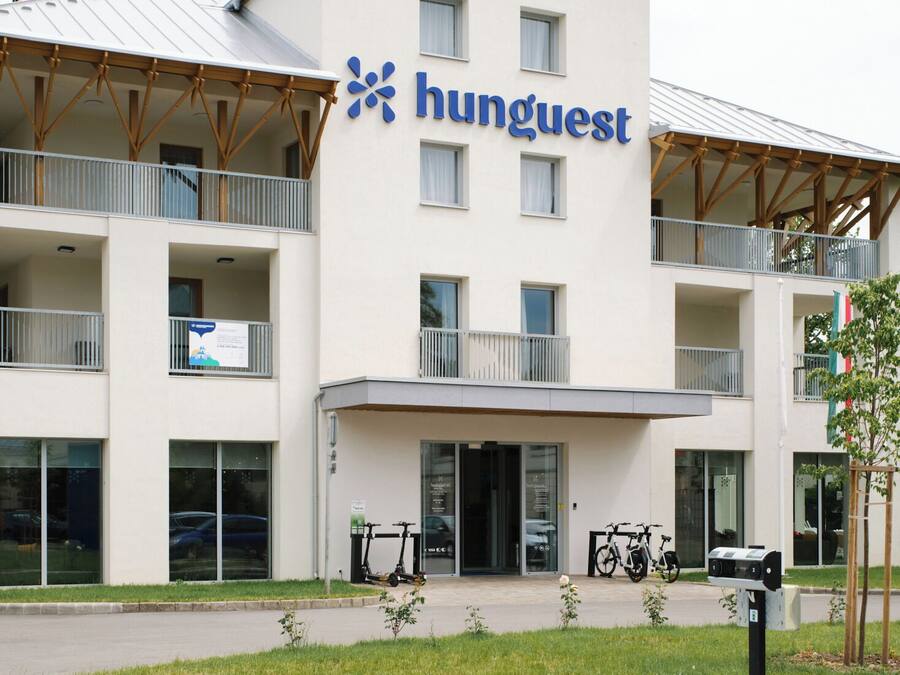 Un edificio de varios pisos con un letrero que dice 'Hunguest' y un espacio de estacionamiento azul con símbolos de silla de ruedas.