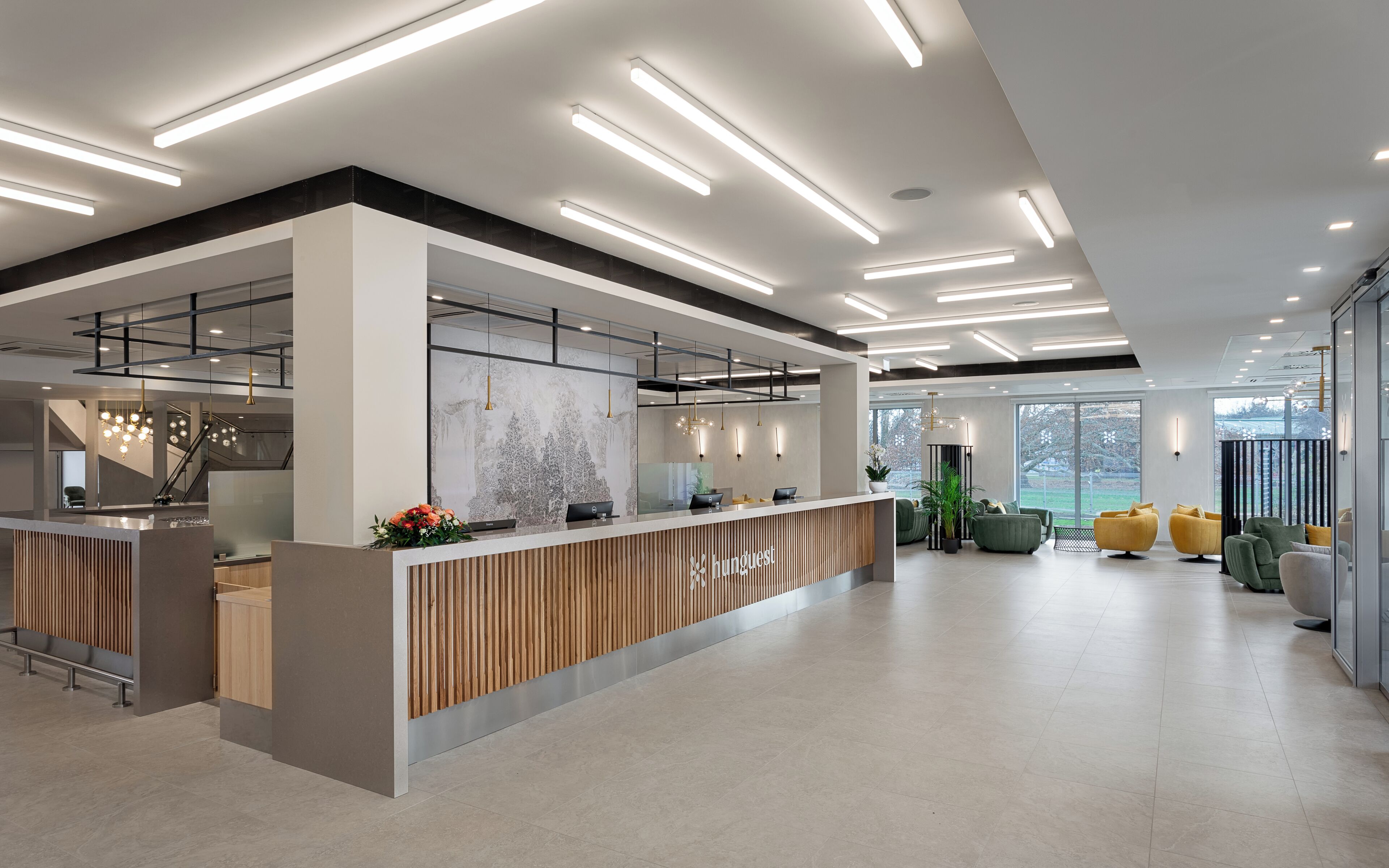 A modern hotel lobby with a reception desk, seating area, and large windows offering a view of the outdoors.