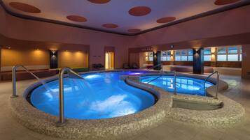 Un'ampia piscina interna con bordo piastrellato, un'area relax con poltrone e un orologio appeso al muro.