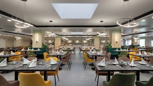 A spacious restaurant with multiple dining tables, chairs, and modern lighting fixtures. - Hunguest Hotel Flora (Eger)